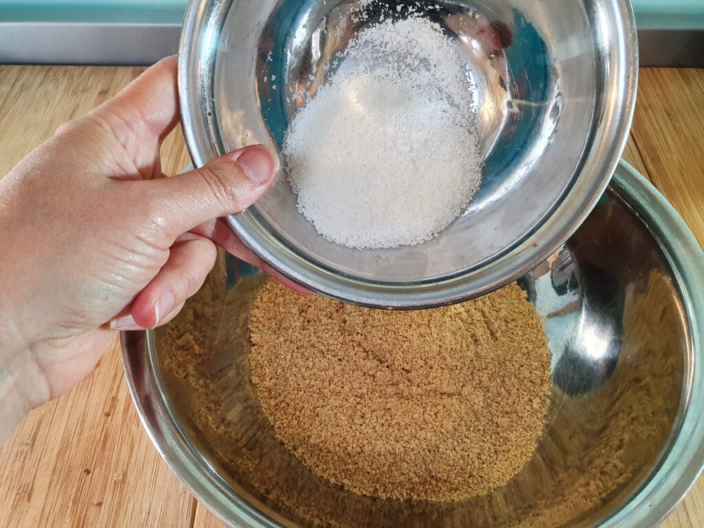 Adding desiccated coconut to biscuit crumbs.