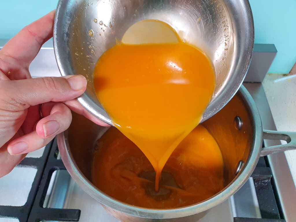 Adding strained passionfruit pulp to pot on stove.