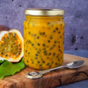 Passion fruit coulis 13 Passion fruit coulis in a glass jar with a vintage spoon in front and fresh, cut open passion fruit and passion fruit leaves on the side, on a wooden chopping board.