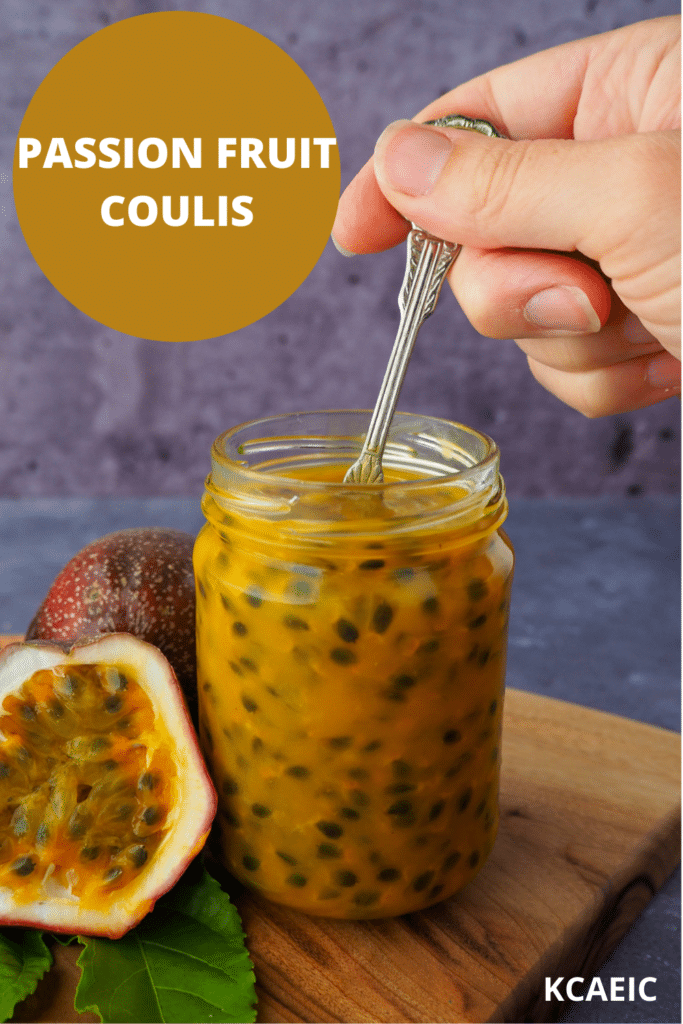 Passion fruit coulis in an glass jar a hand holding a vintage spoon in the jar and fresh, cut open passion fruit and passion fruit leaves on the side, on a wooden chopping board, with text overlay Passion fruit coulis, KCAEIC