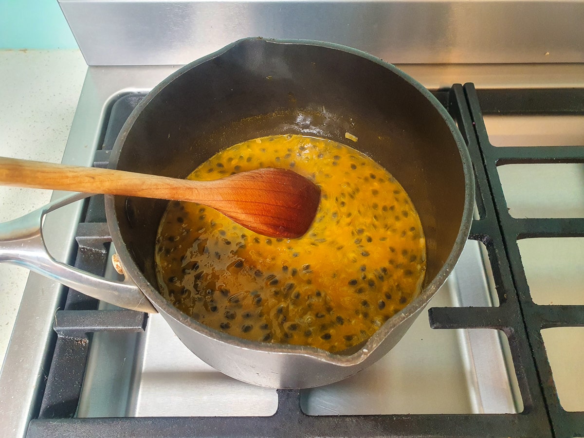 Stirring passion fruit coulis in pot on stove.