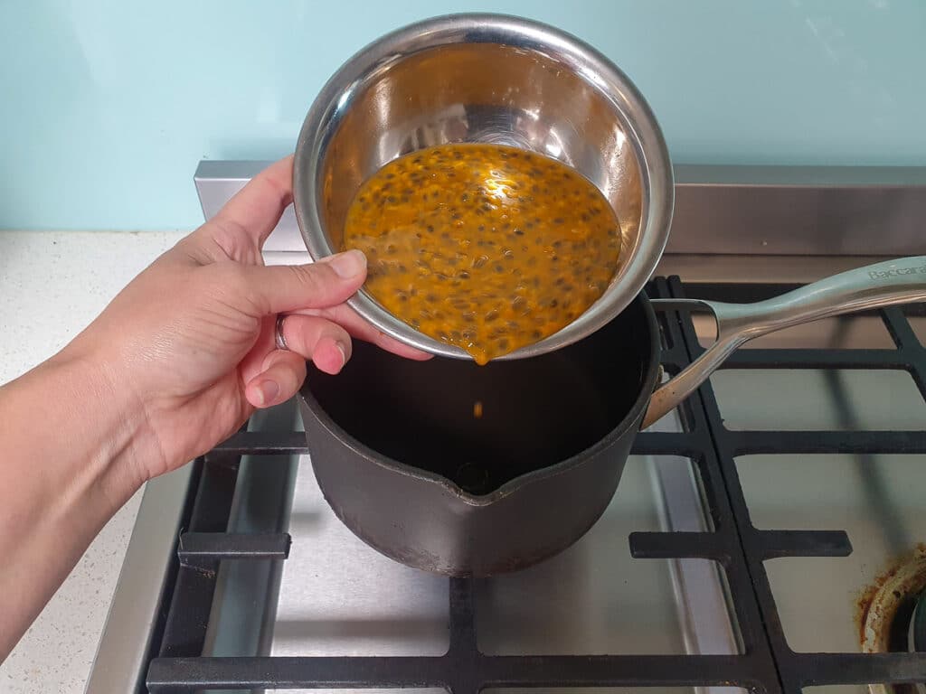 Adding passion fruit pulp to pot on stove.