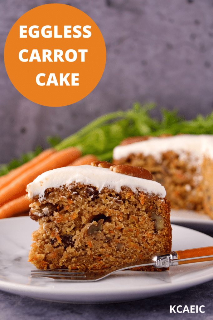 Slice of eggless carrot cake decorated with lemon icing and pecans on a plate with a vintage fork and the rest of the cake and fresh Dutch carrots in the background and text overlay, eggless carrot cake, KCAEIC.