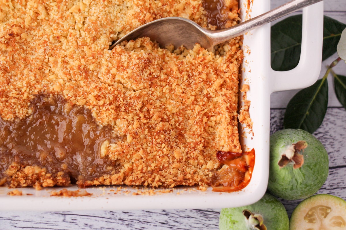 Top down view of feijoa crumble in a baking dish with a vintage serving spoon and fresh feijoa on the side.