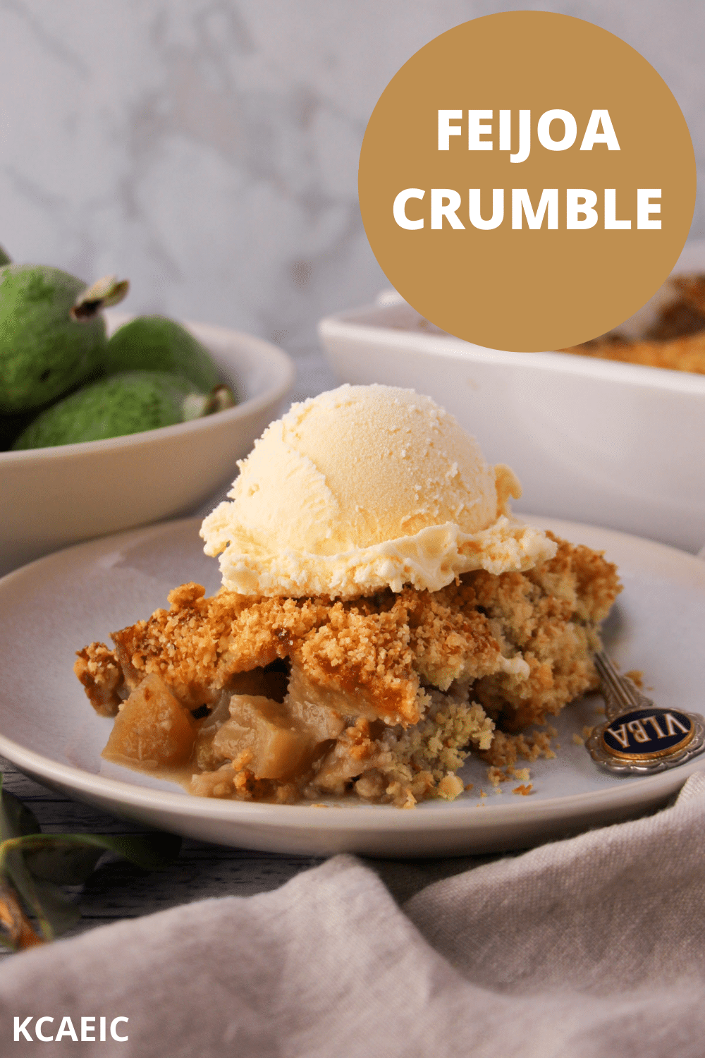 Feijoa crumble on a plate with ice cream and a spoon, with text overlay, feijoa crumble, KCAEIC.