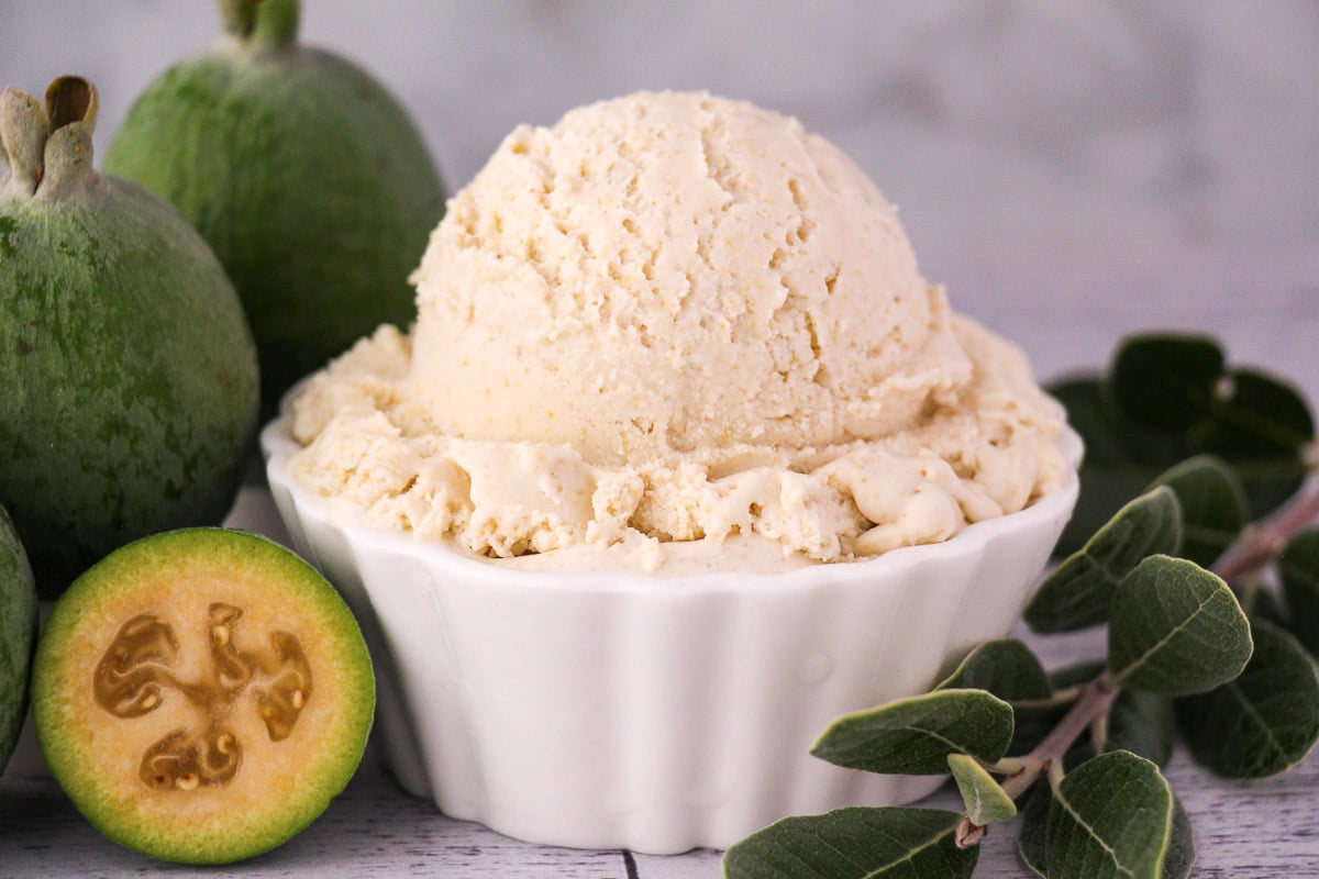 Scoop of feijoa ice cream with fresh feijoa, cut in half feijoa and sprig of feijoa leaves.