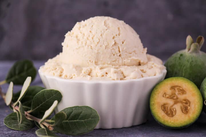 Scoop of feijoa ice cream with fresh feijoa, cut in half feijoa and sprig of feijoa leaves.