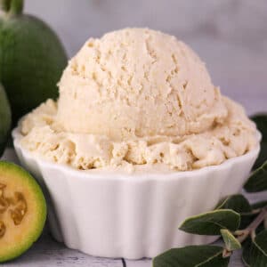 Close up scoop of feijoa ice cream with fresh feijoa, cut in half feijoa and sprig of feijoa leaves.