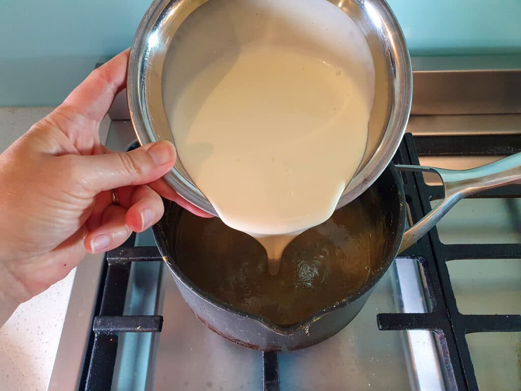 Adding cream to ice cream mix in pot on stove.