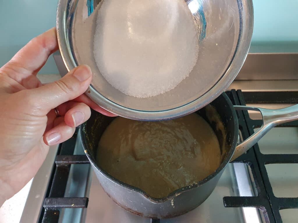 Adding sugar to ice cream mix in pot on stove.