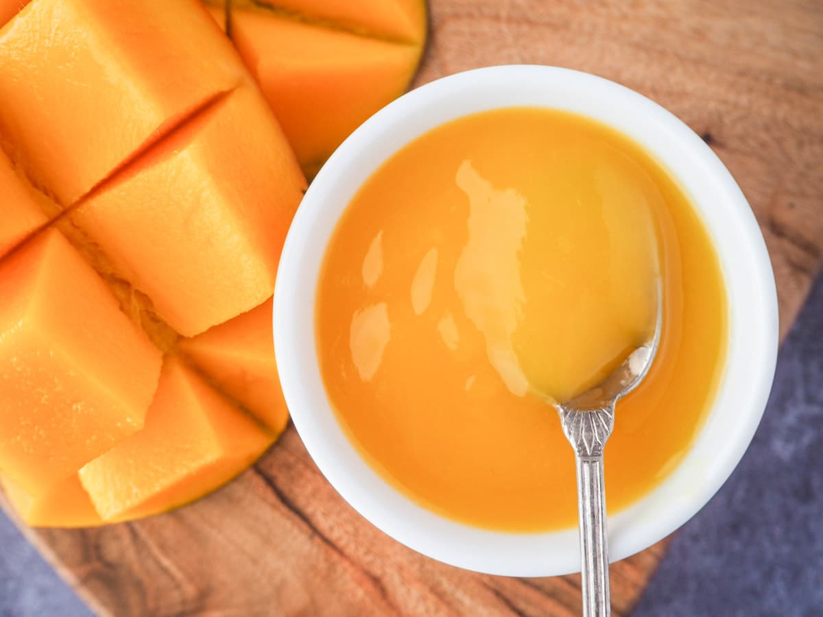 Mango coulis in a serving bowl with vintage spoon and fresh mango on the side.