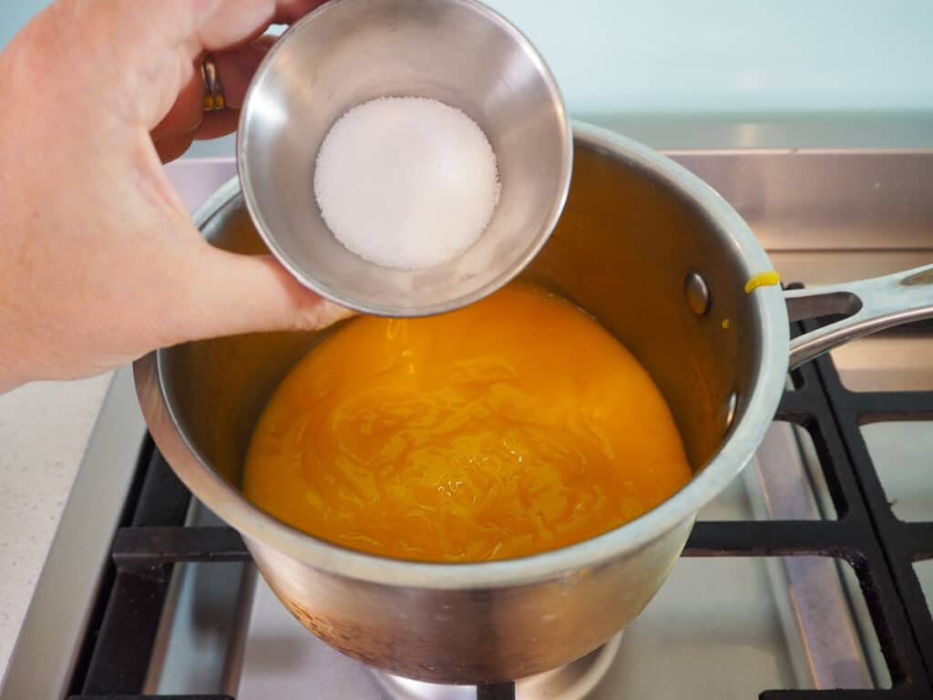 Adding sugar to strained mango in pot.