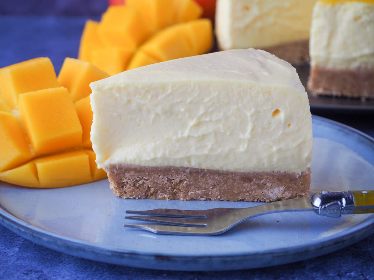 Slice of no bake mango cheesecake with a vintage fork and fresh mango on the side.