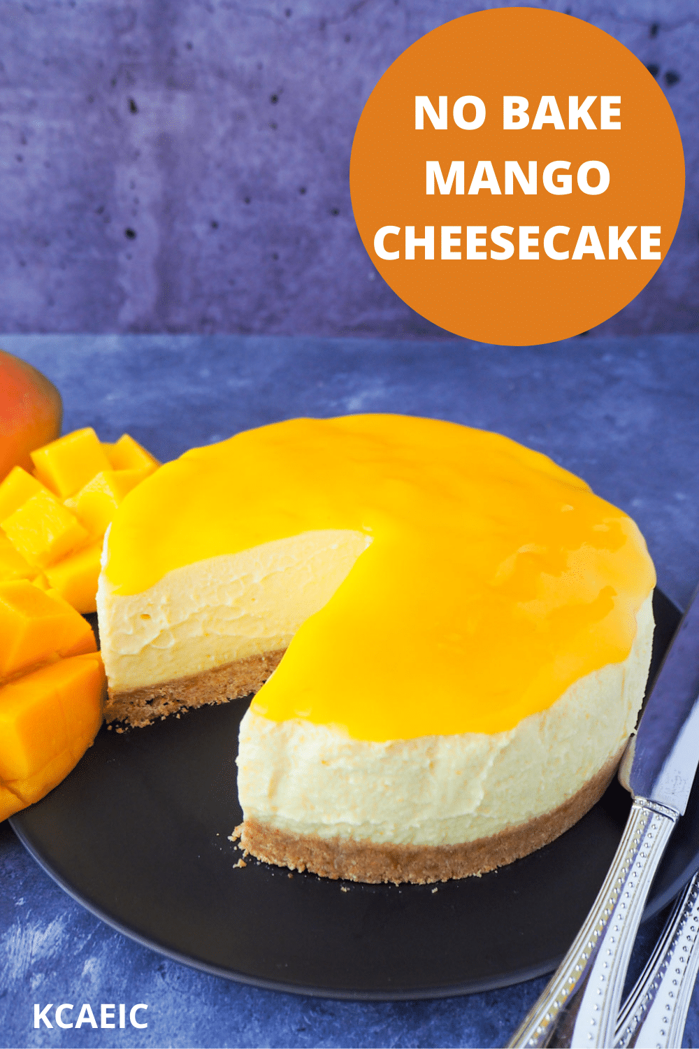 No bake mango cheesecake with a single slice cut out, mango coulis, fresh mango and silver serving wear, with text overlay, no bake mango cheesecake and KCAEIC.