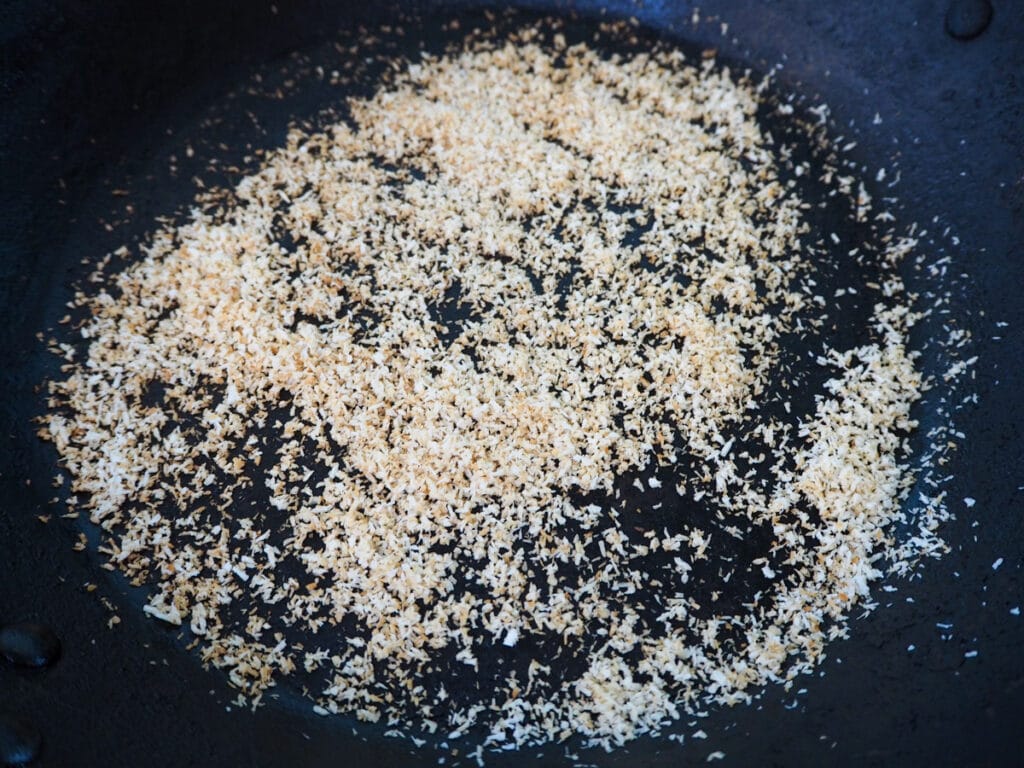 Desiccated coconut in pan starting to go golden brown color, ready to take off heat.