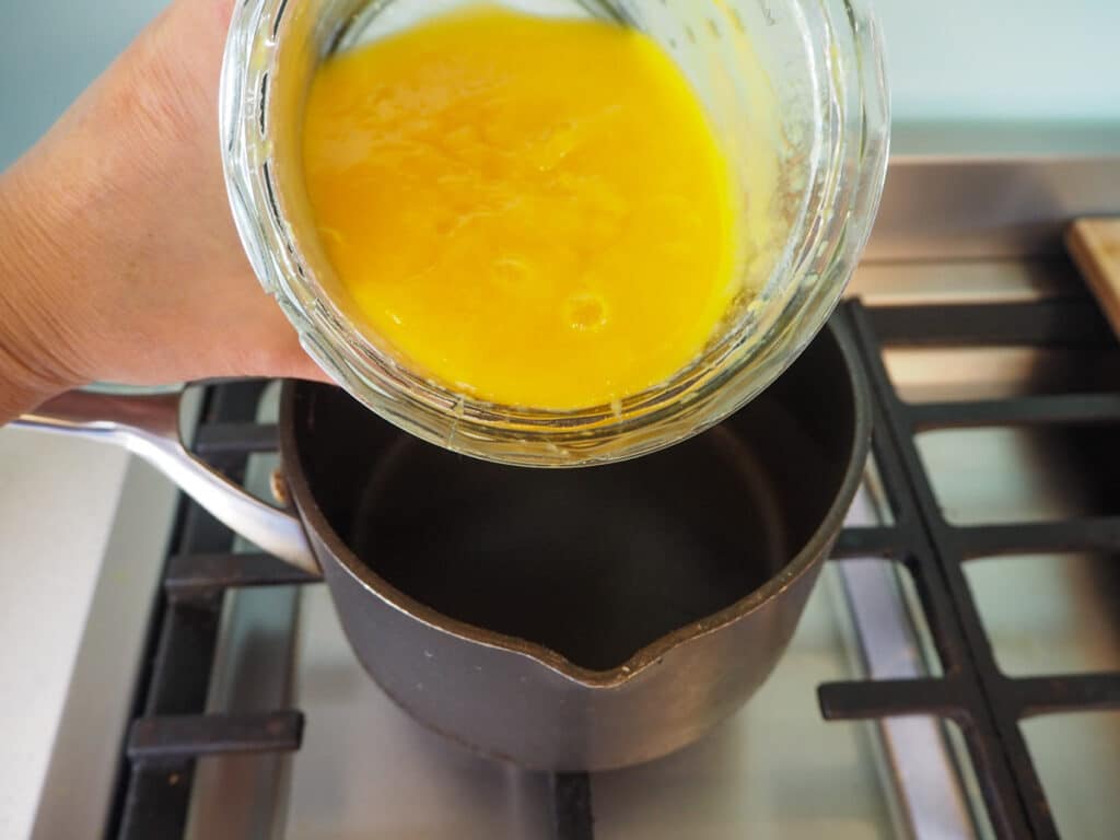 Tipping mango puree and agar agar mix into small pot on stove.