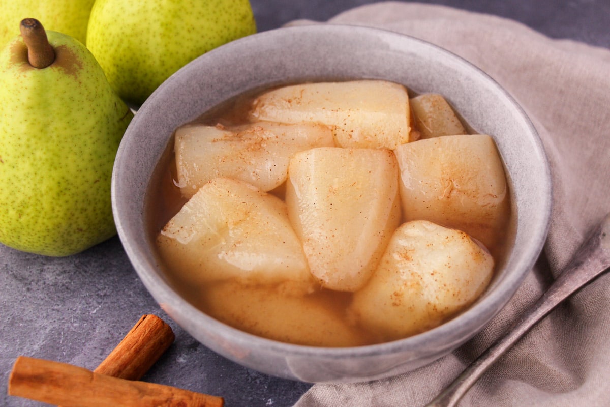 Stewed pears 2 Stewed pears in a bowl, with fresh pears, cinnamon sticks and a vintage serving spoon on the side.
