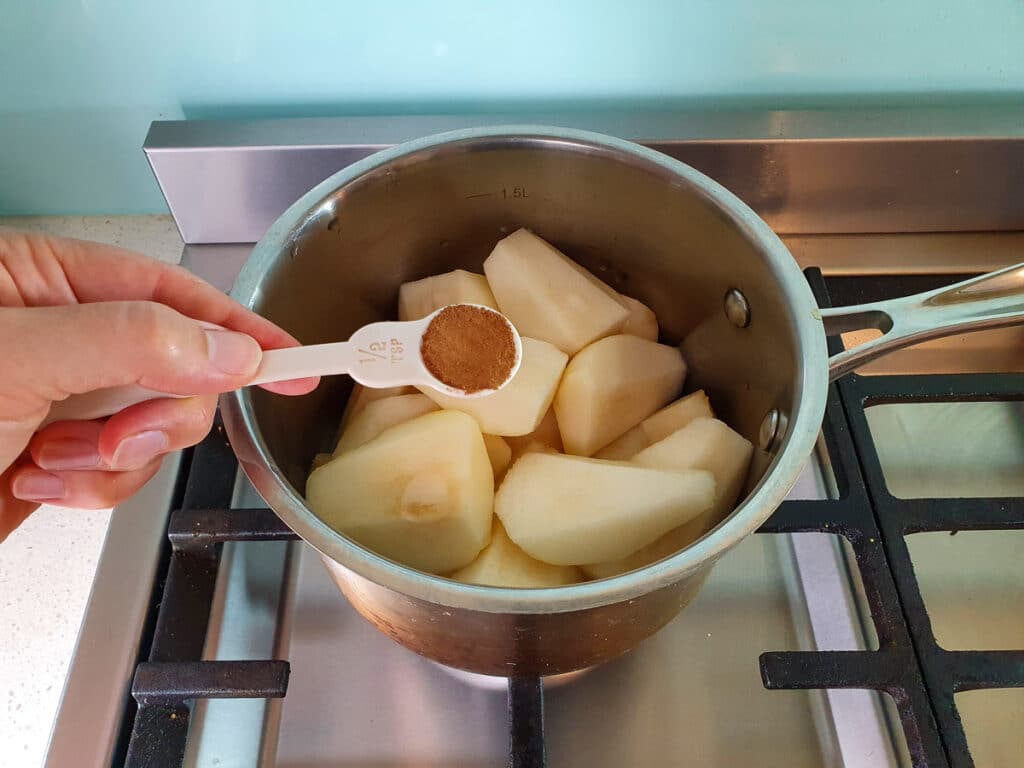 Sprinkling cinnamon over pears in pot on stove.