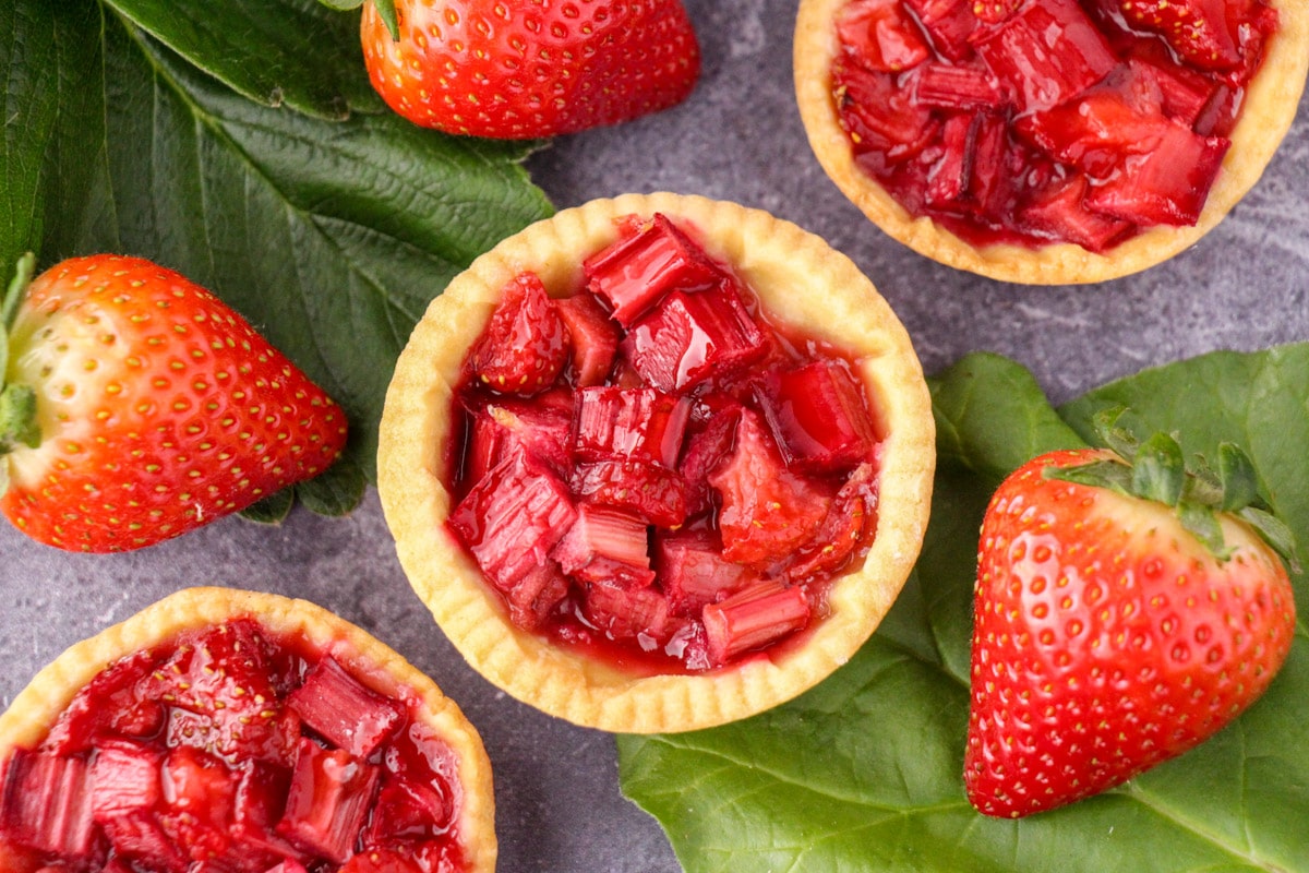 Close up strawberry rhubarb tartlets with strawberry and rhubarb leaves and fresh strawberries.