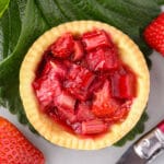 Close up strawberry rhubarb tartlets with strawberry leaves and fresh strawberries on the side.
