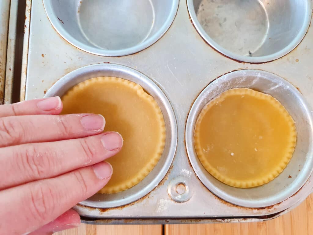 Gently pushing pastry into muffin tins with fingers.