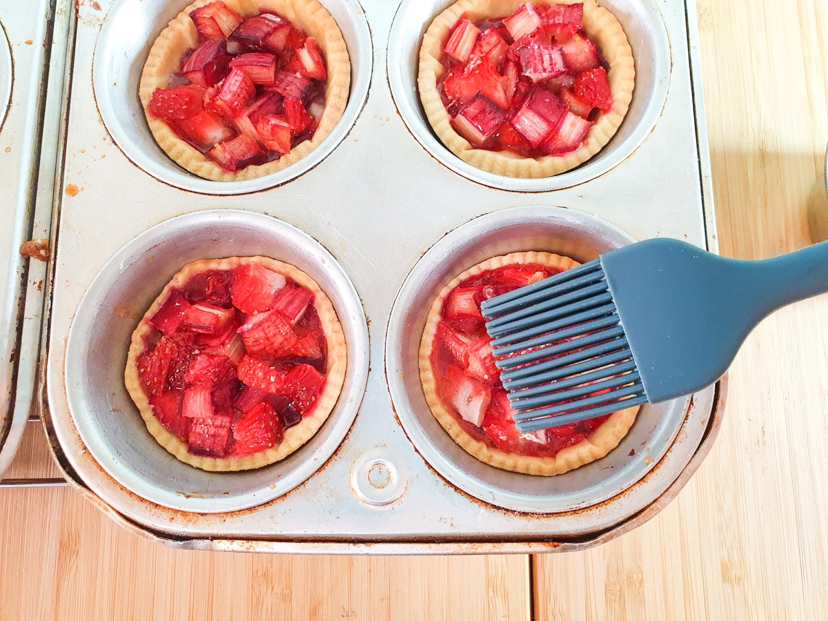 Brushing strawberry jam onto just baked tartlets.