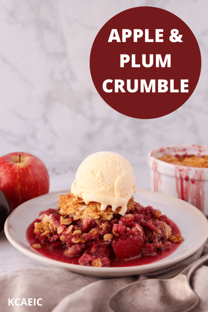 Apple and plum crumble on a plate with ice cream, with vintage serving spoon and ramakin and fresh fruit in the back ground and text overlay, apple and plum crumble and KCAEIC.