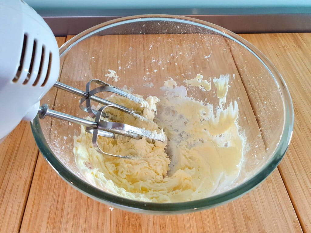 Feijoa cake 18 Beating cake icing with a hand held electric beaters.