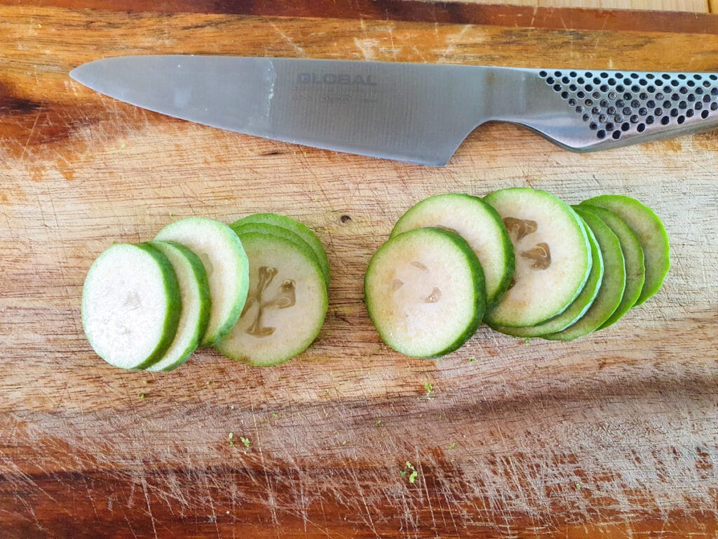 Slicing fresh feijoas into thick coins to decorate cake.