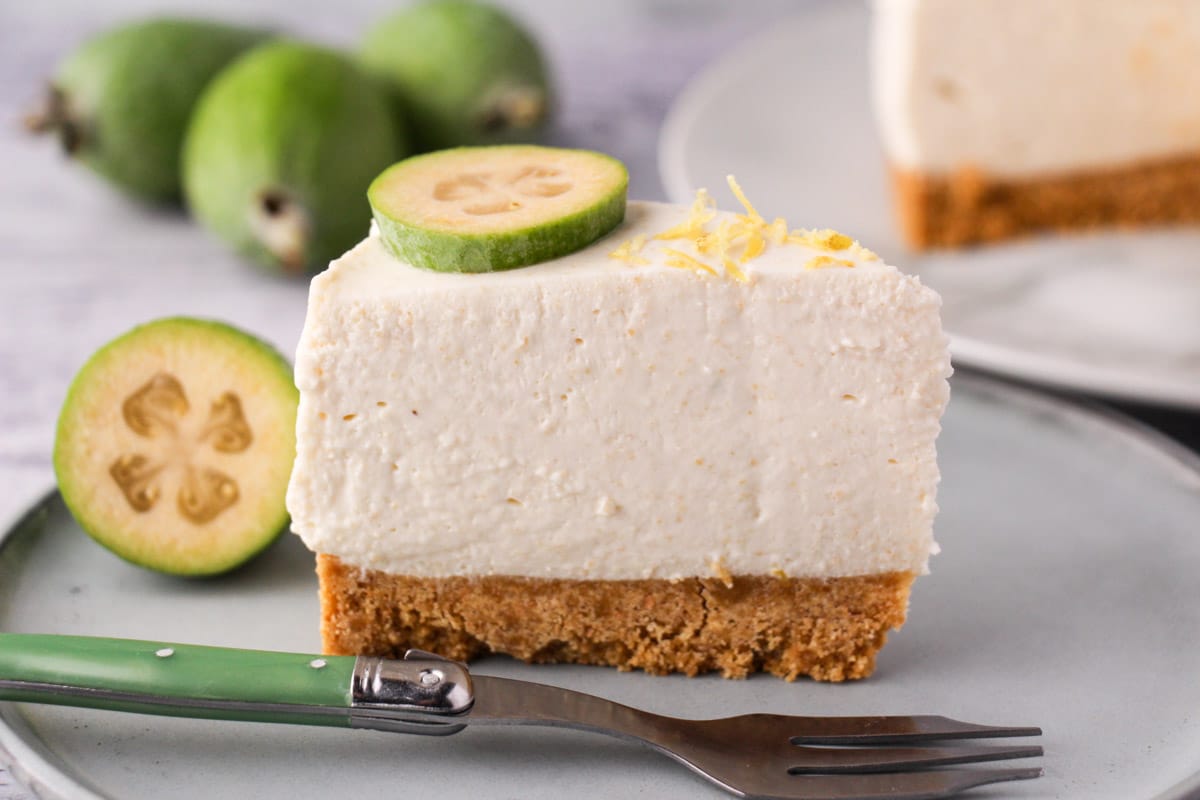 Slice of feijoa cake on the serving plate with vintage spoon, rest of cake and fresh feijoas in the background.