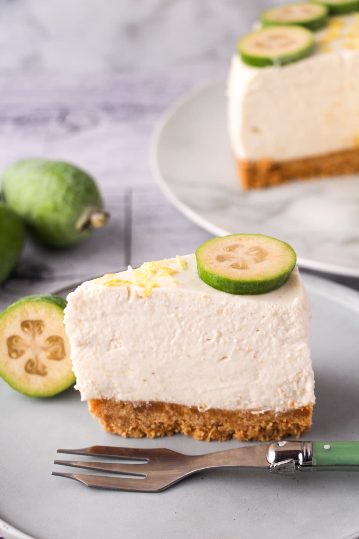 Slice of feijoa cake on the serving plate with vintage spoon, rest of cake and fresh feijoas in the background.