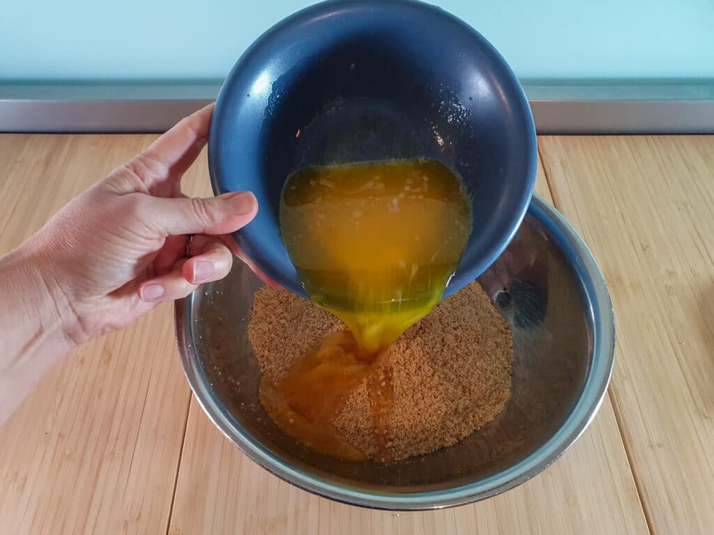 Adding melted butter to biscuit crumbs.