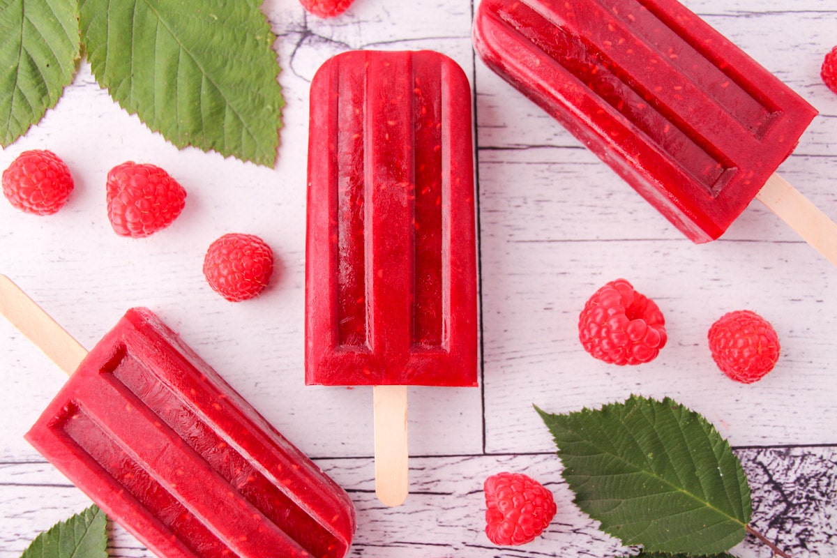 Raspberry popsicles with fresh raspberries and leaves.