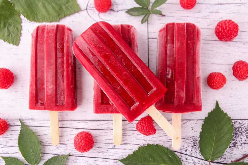 Stacked raspberry popsicles with fresh raspberries and leaves.