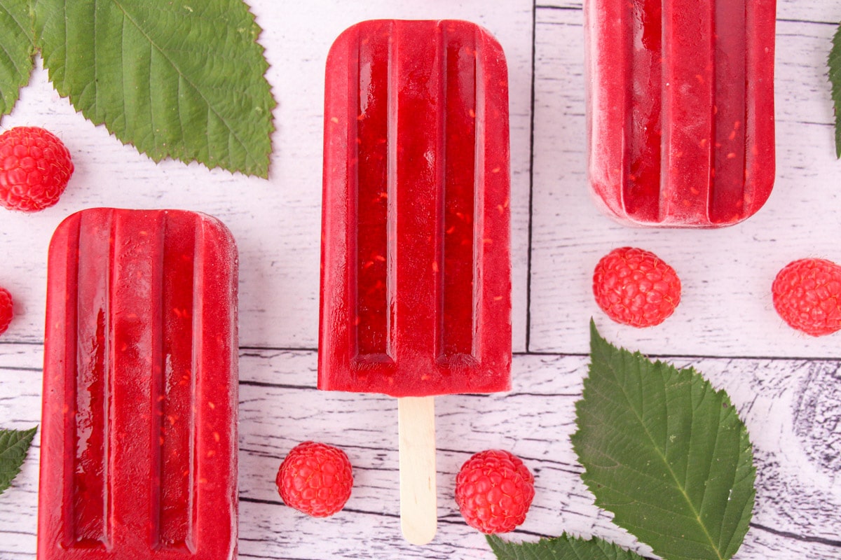 Raspberry popsicles with fresh raspberries and leaves.