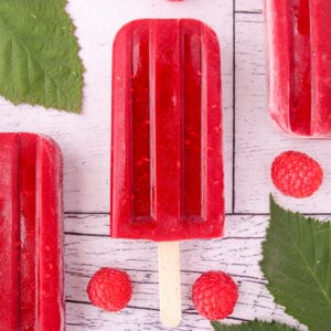 Close up raspberry popsicles with fresh raspberries and leaves.