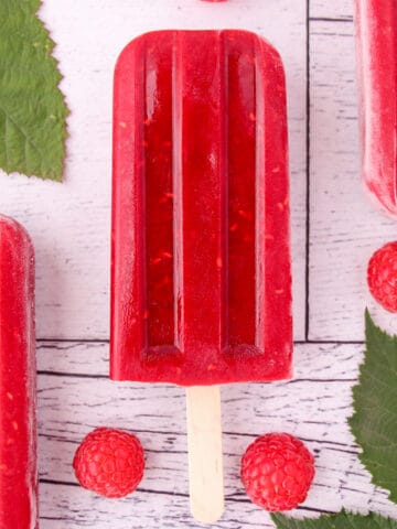 Close up raspberry popsicles with fresh raspberries and leaves.