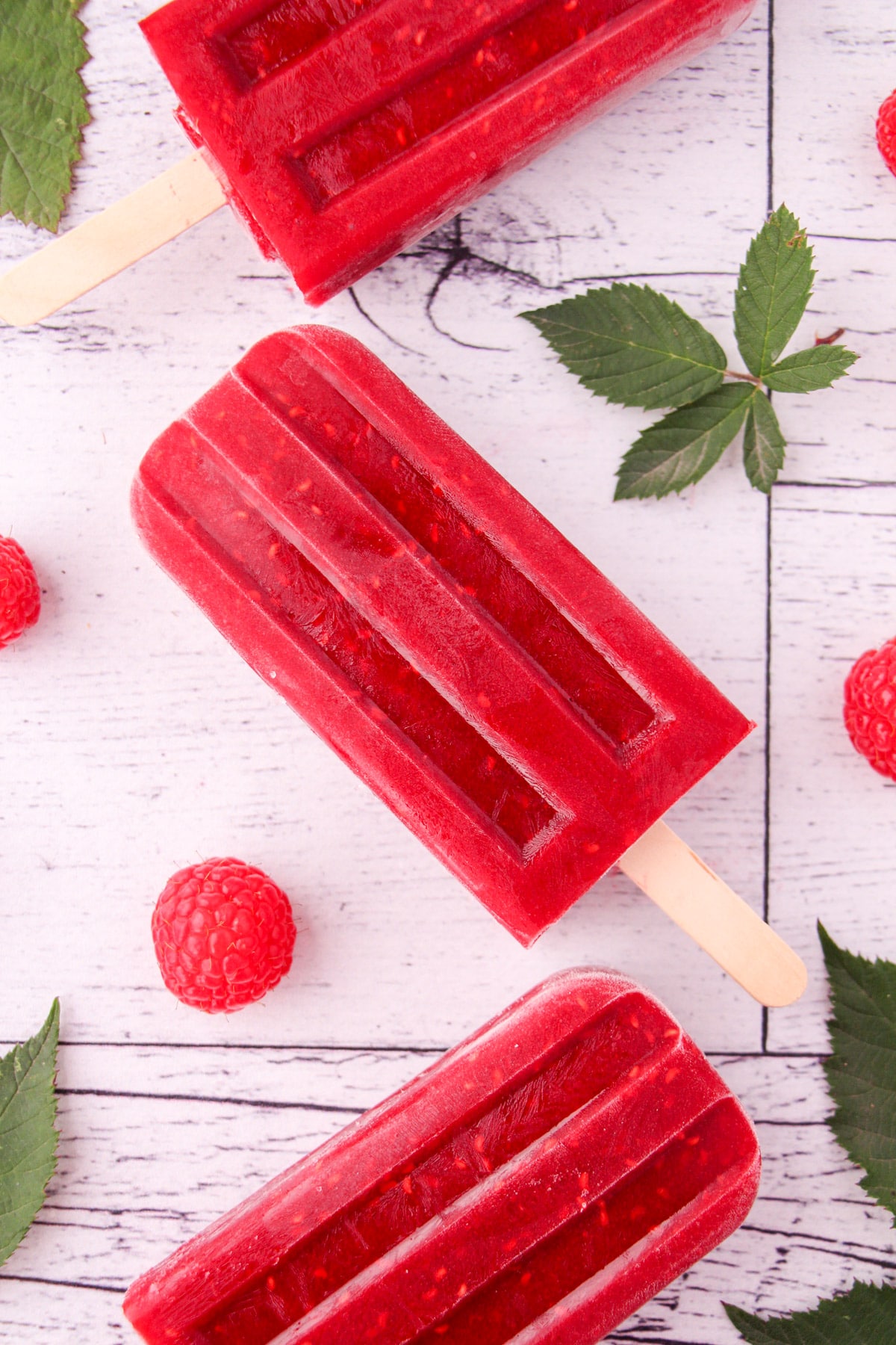 Raspberry popsicles with fresh raspberries and leaves.