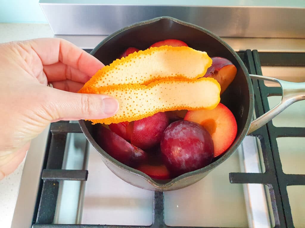 Adding strips of orange zest to plums.