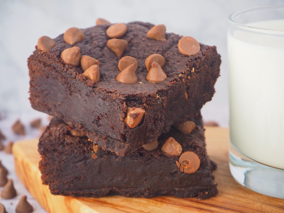 Stack of eggless brownies on a board with a glass of milk.