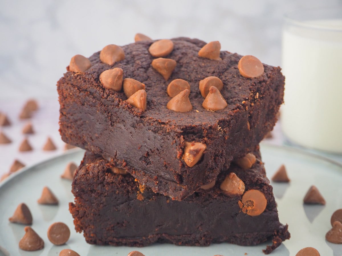 Stack of eggless brownies on a plate with a glass of milk in the background.