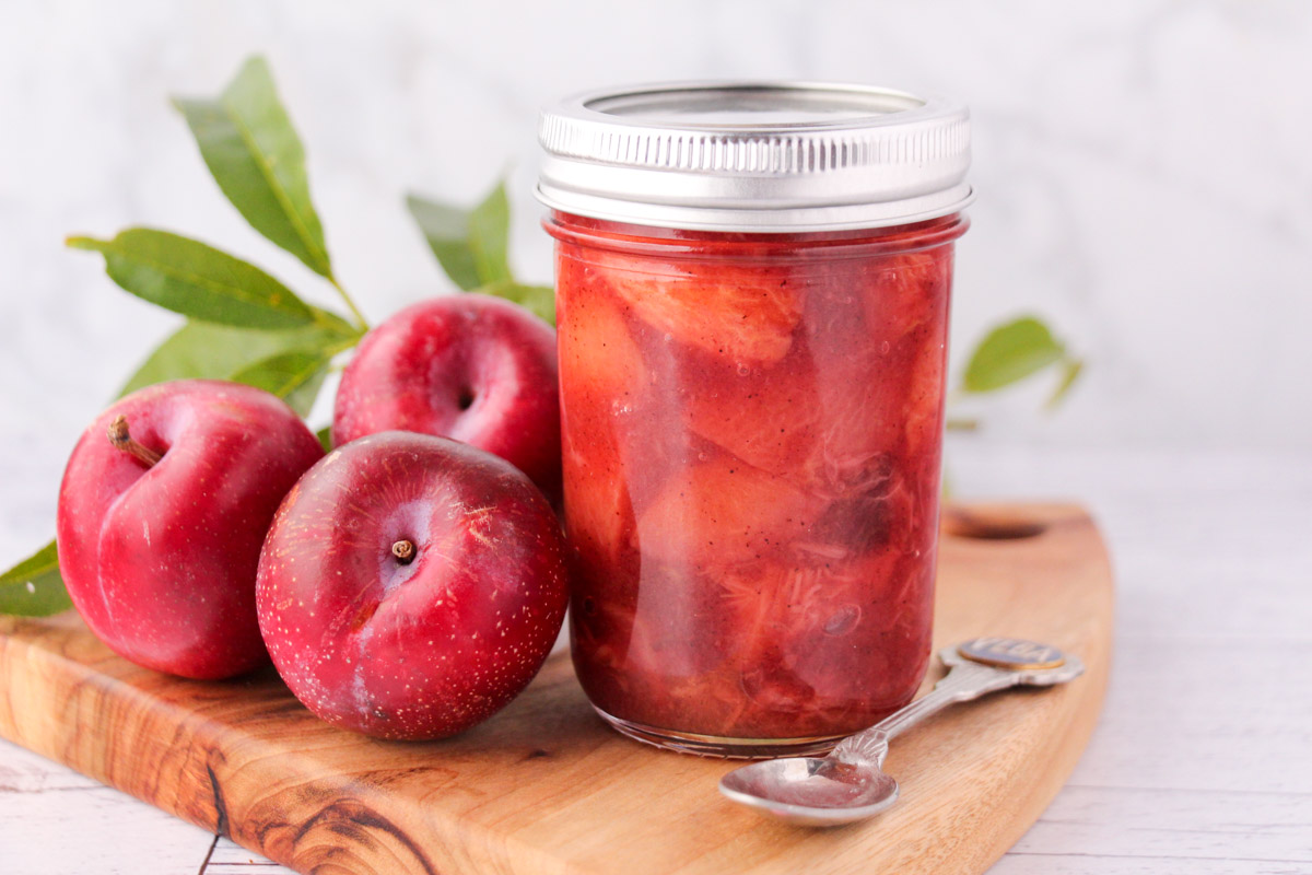 Plum compote in a mason jar with a vintage spoon, fresh plums and leaves on the side.