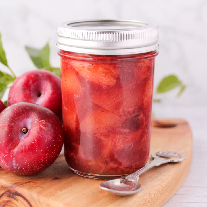 Close up mason jar of plum compote with fresh plums and leave and a vintage spoon.