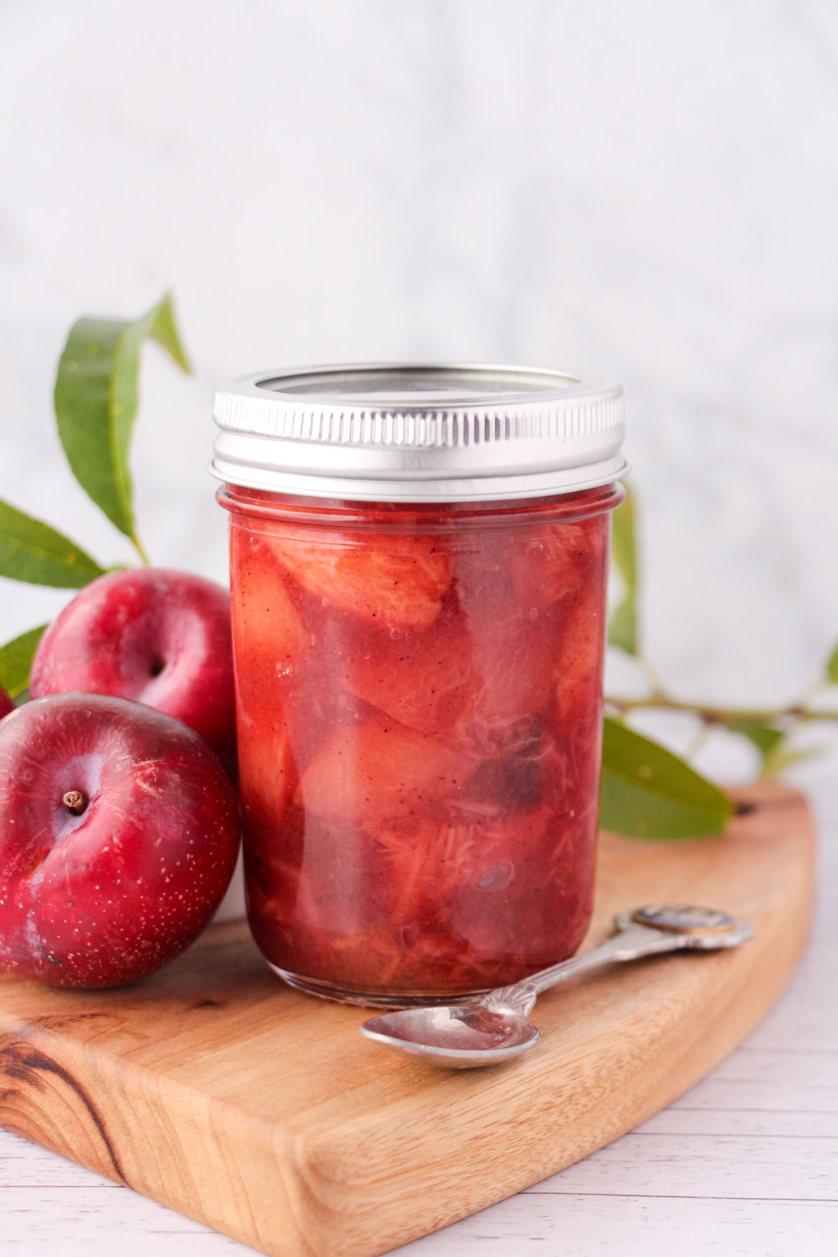 Plum compote in a mason jar with a vintage spoon, fresh plums and leaves on the side.