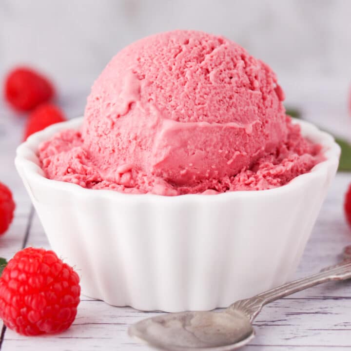 Close up of scoop of raspberry ice cream in a bowl, with fresh raspberries on the side and a vintage spoon.