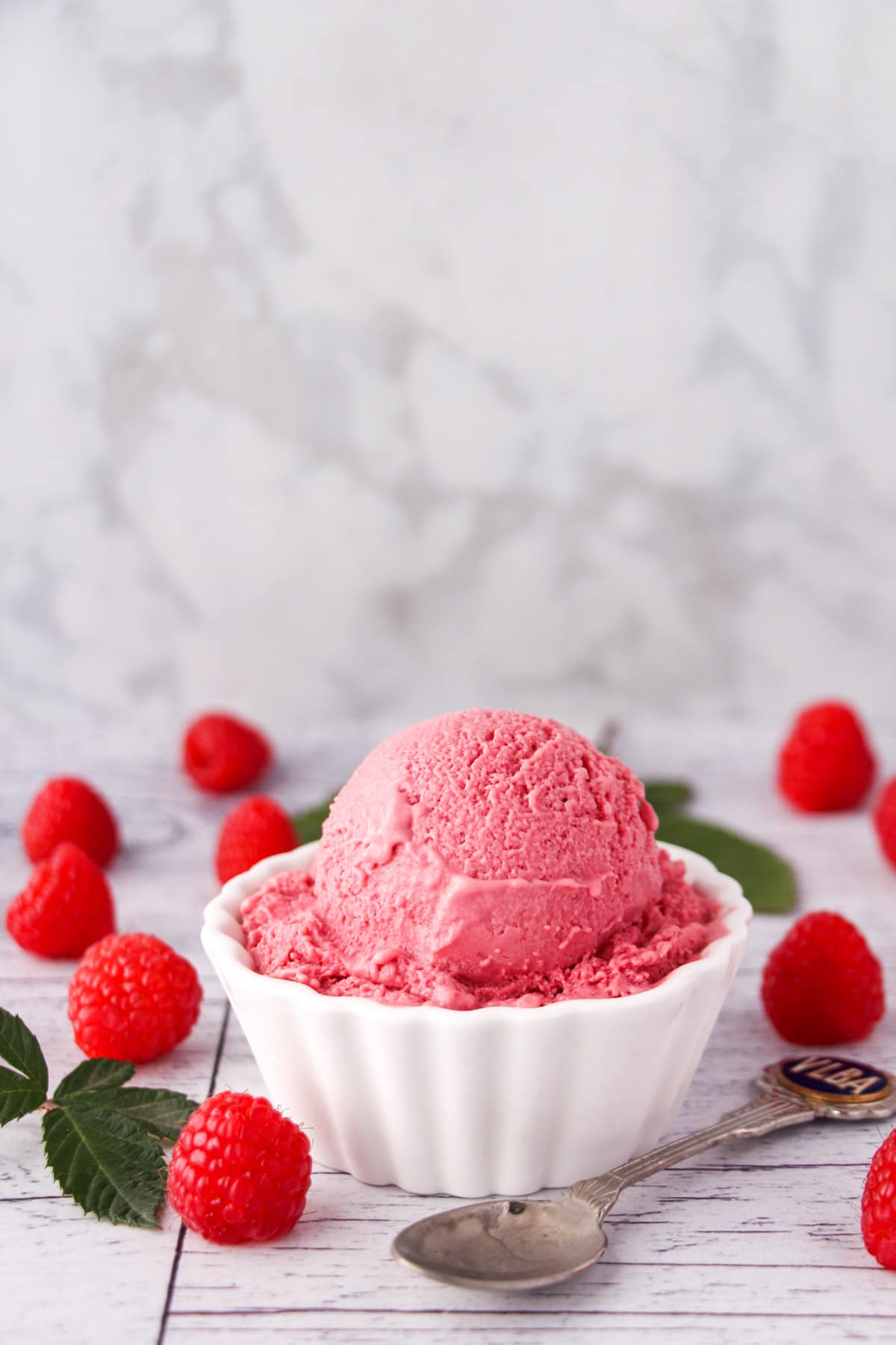 Raspberry ice cream 24 Scoop of raspberry ice cream in a bowl, with fresh raspberries and leaves on the side and a vintage spoon.