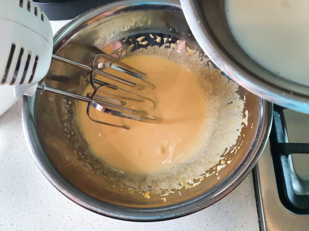 Adding warmed milk to blended egg yolks and sugar.