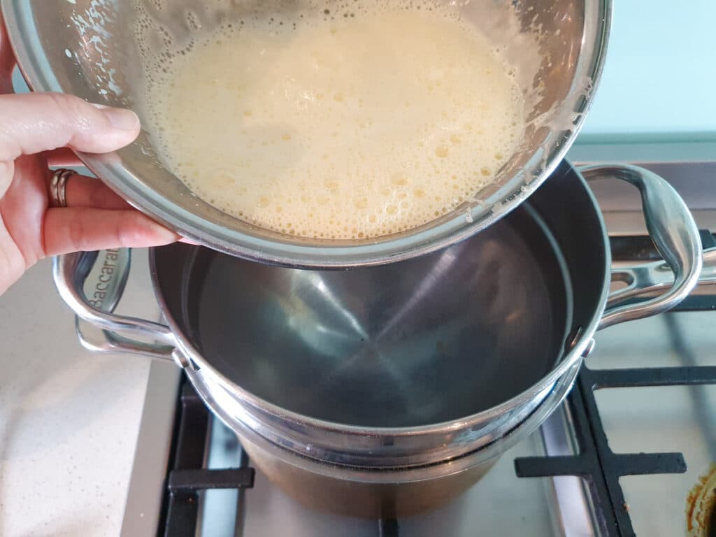 Adding egg mix to top of double boiler.