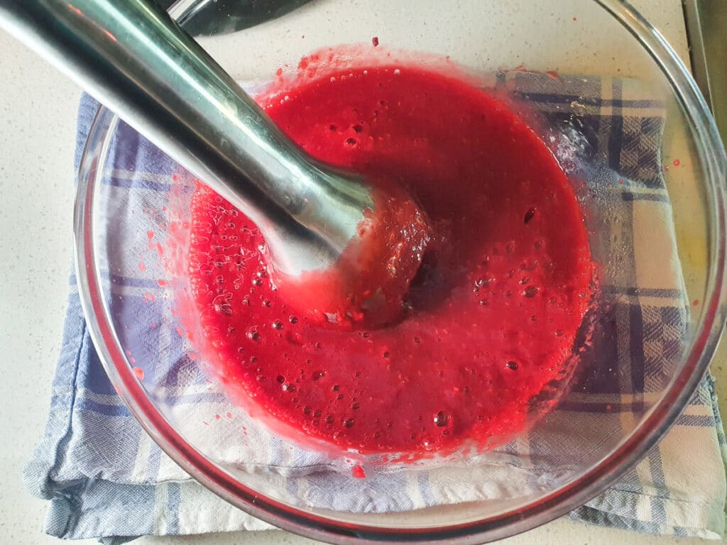 Blending raspberries with an immersion blender.