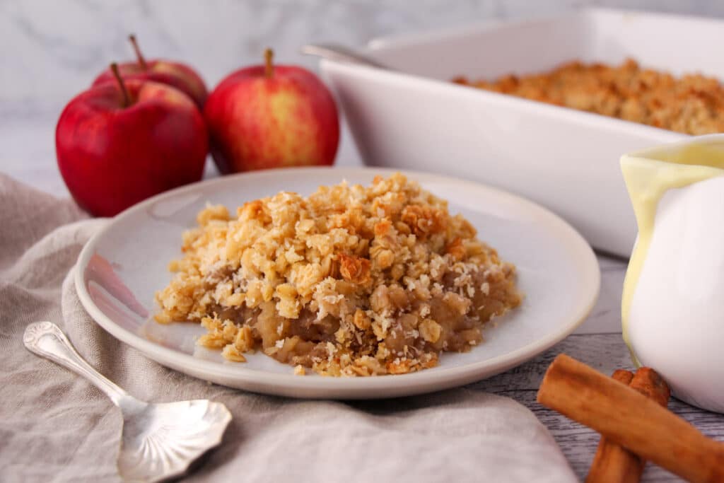 Vegan apple crumble, with fresh apples and baking dish in the background.